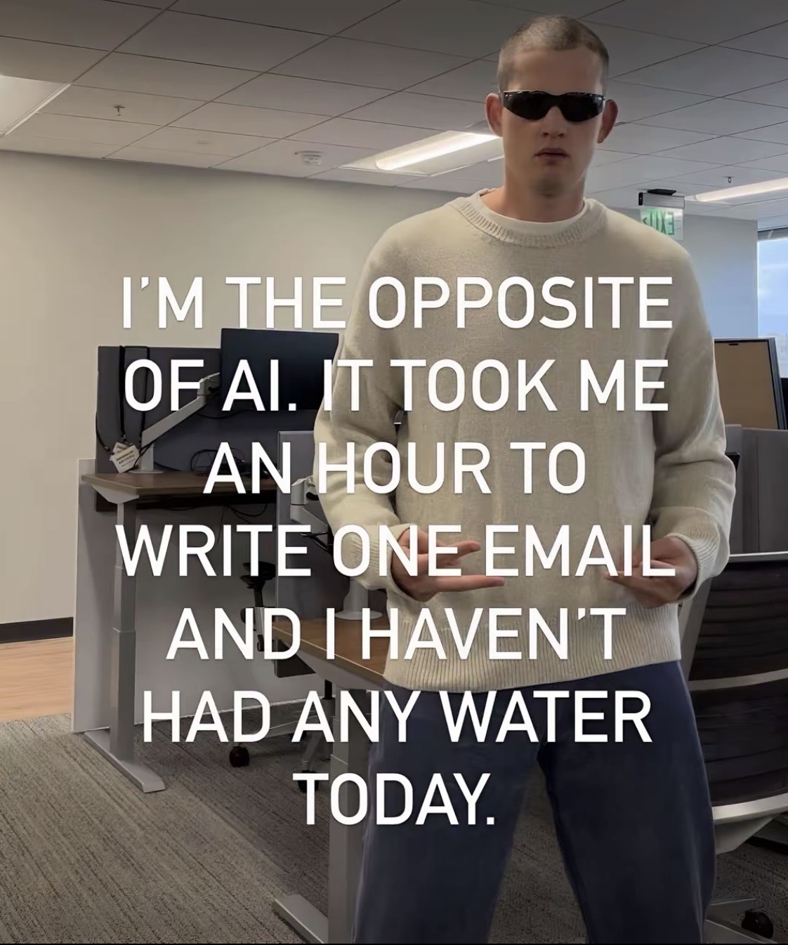 Photo of a person in an office standing up wearing sunglasses with the caption “I'M THE OPPOSITE OF AI. IT TOOK ME AN HOUR TO WRITE ONE EMAIL AND I HAVEN'T HAD ANY WATER TODAY.”